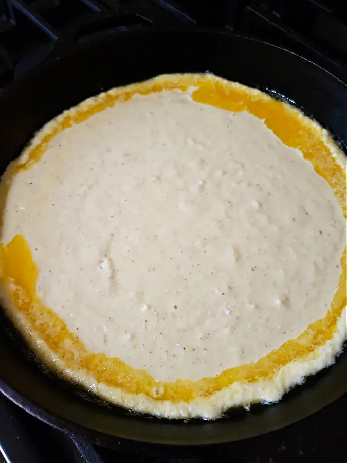 hot cast iron skillet with melted butter and cornbread batter ready for the oven
