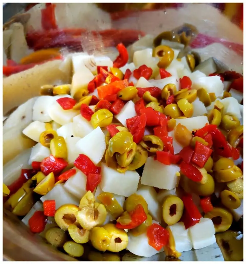 Silver mixing bowl with ingredients to prepare potato salad with olives