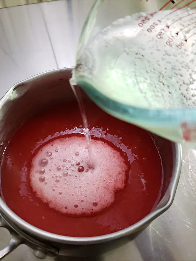 pouring cold carbonated 7up into hot strawberry gelatin applesauce mixture in a pot
