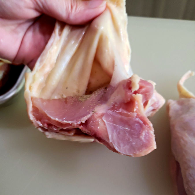 lifting the skin of a chicken thigh to add seasoning directly to the dark meat of the poultry.