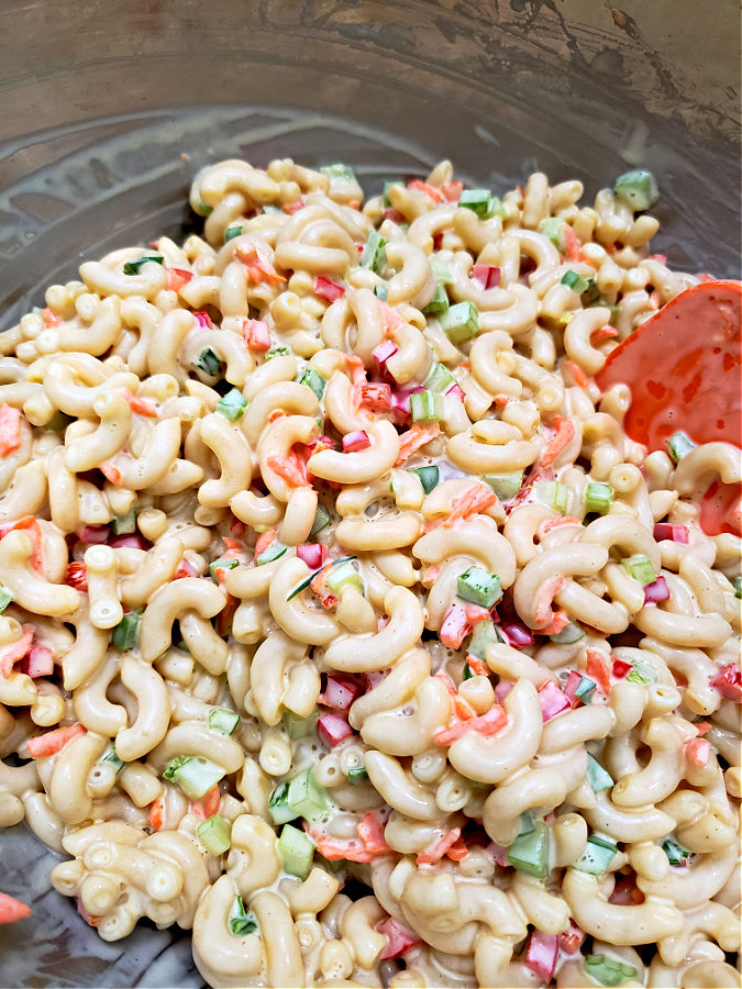 stainless mixing bowl combining macaroni salad recipe ingredients together with a silicone spatula