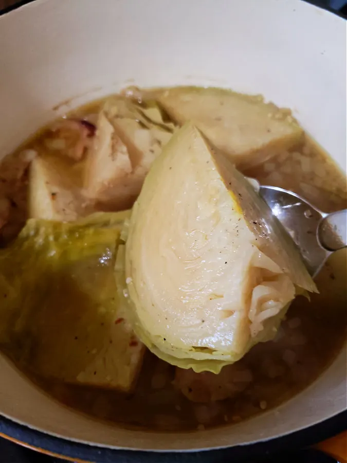 Using a serving spoon to hold up a wedge of tender cabbage boiled southern style